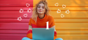 Eine junge Frau sitzt mit Laptop auf dem Boden und blickt gespannt in die Kamera